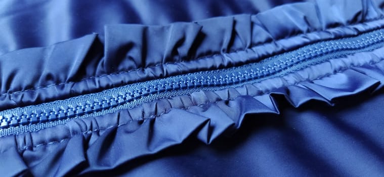 Buttoned zip on a blue raincoat. Waves and folds in the fabric. Beautiful flounces, ruffles, frills. Decorative finishing of a garment. Smocked, sewn silk fabric. Nice casual wear