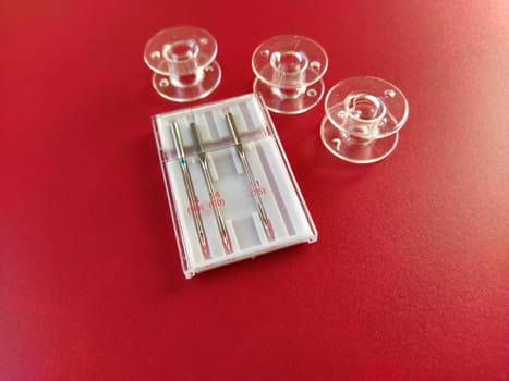 plastic bobbins and a set of sewing machine needles on a red background.