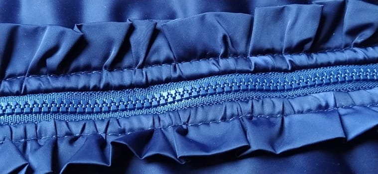 Buttoned zip on a blue raincoat. Waves and folds in the fabric. Beautiful flounces, ruffles, frills. Decorative finishing of a garment. Smocked, sewn silk fabric. Nice casual wear, banner