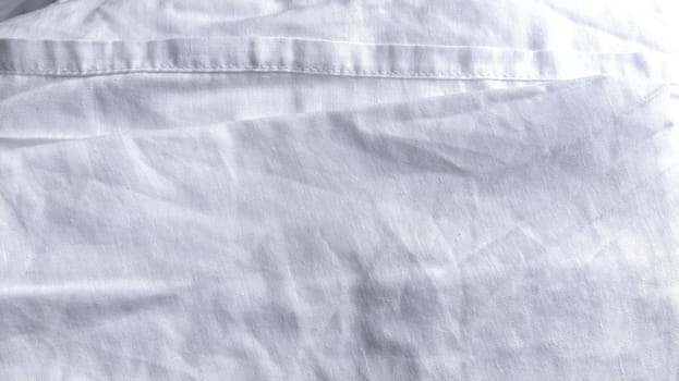 White cotton fabric, not ironed and crumpled in waves. White background. Tablecloth or sheet. The edge is hemmed with a sewing machine. Laundry after washing. Cotton Fabric Texture.