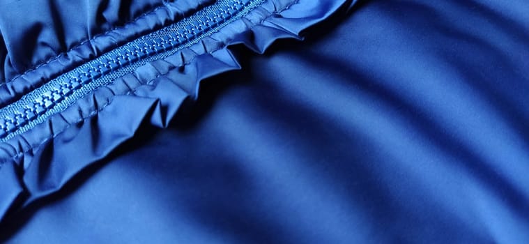 Buttoned zip on a blue raincoat. Waves and folds in the fabric. Beautiful flounces, ruffles, frills. Decorative finishing of a garment. Smocked, sewn silk fabric. Nice casual wear