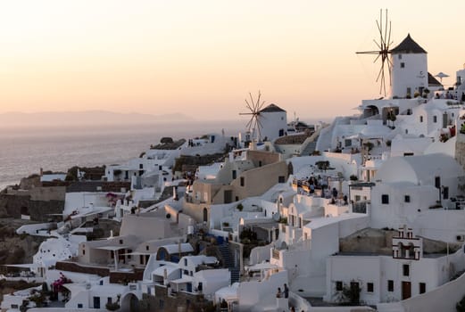 Oia, Santorini, Greece - June 28, 2021: Whitewashed houses and windmills in Oia in warm rays of sunset on Santorini island. Greece
