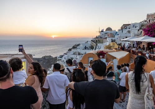 Oia, Santorini, Greece - June 28, 2021: Tourists looking at the sunset in Oia, Santorini, Cyclades, Greece