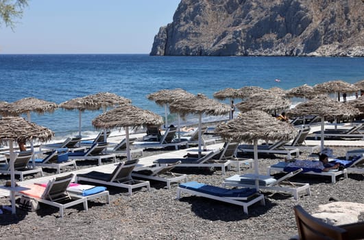 Kamari, Santorini, Greece - June 30, 2021: Sun loungers on the black volcanic beach of Kamari in Santorini. Cyclades, Greece