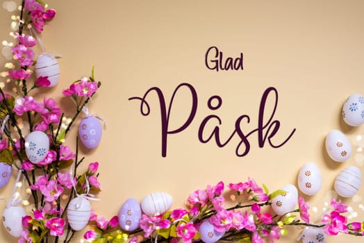 Swedish Text Glad Pask Means Happy Easter On Beige Background. Pink And Purple, Shiny And Bright Spring Flower Arrangement With Easter Egg Decoration.