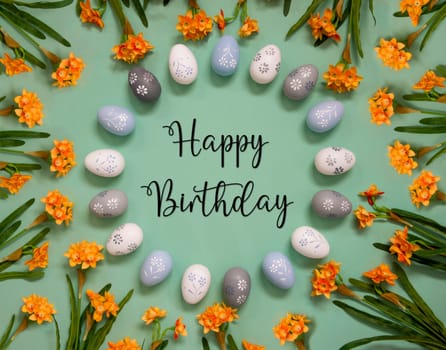 Flat Lay With English Text Happy Birthday. Easter Egg Decoration With Orange Spring Flowers. Light Green Paper Background.