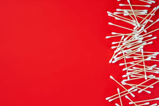 Wooden cotton buds on red background. Hygienic accessory product concept. Environmental conservation concept. Auricle hygiene. Beauty concept. Top view. Flat lay.