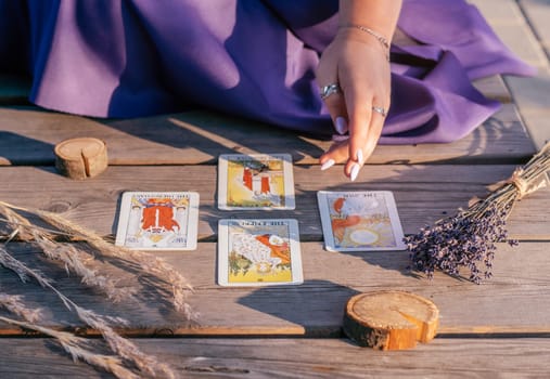 Woman's hand with purple nails points to four Tarot cards spread out on wooden surface next to spikelets and lavender. Minsk, Belarus - 07.28.2021