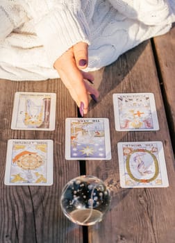 Woman's hand with purple nails points to five Tarot cards spread out on wooden surface next to crystal ball. Vertical. Minsk, Belarus - 07.28.2021