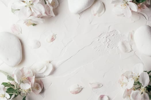 Delicate background of apple flowers, petals and pebble stones lying on white gypsum plaster. Top view. Copy space