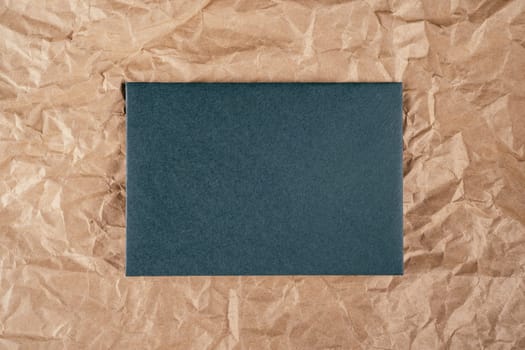 Background image of rough crumpled recycled textured kraft paper with sheet of dark green cardboard in middle. Top view. Copy space