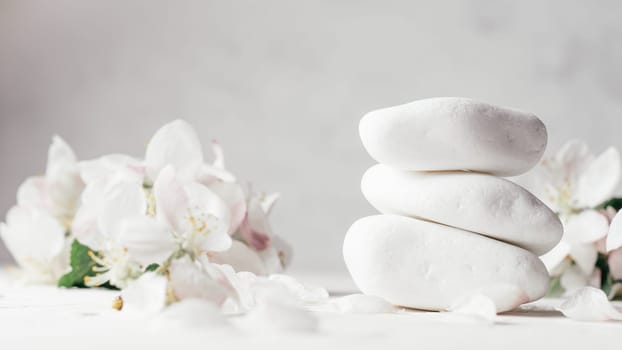 Stack of white pebble stones on light plaster surface with apple flowers. Banner
