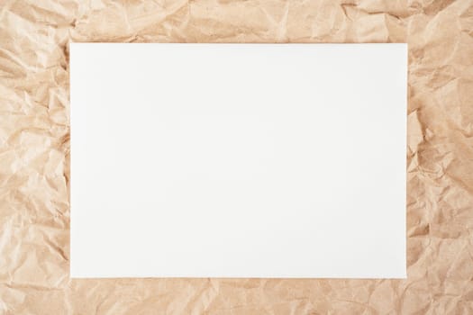 Background image of rough crumpled recycled textured kraft paper with sheet of white cardboard in middle. Top view. Copy space
