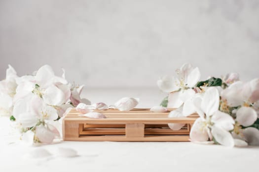 Wooden podium in form of pallet on light plaster surface with apple flowers. Podium, pedestal or stage. Mockup for cosmetic products