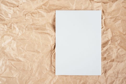 Background image of rough crumpled recycled textured kraft paper with sheet of white cardboard on side. Top view. Copy space