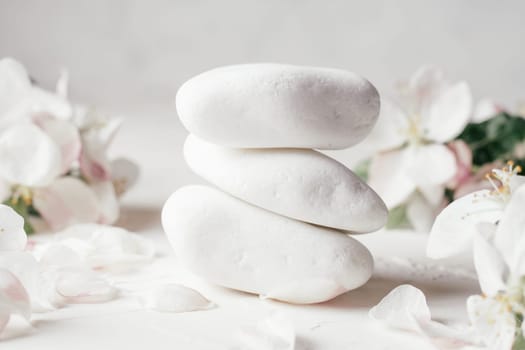 Stack of white pebble stones on light plaster surface with apple flowers