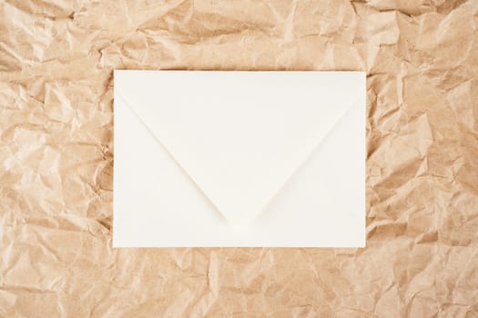 Background image of rough crumpled recycled textured kraft paper with white cardboard envelope in middle. Top view. Copy space