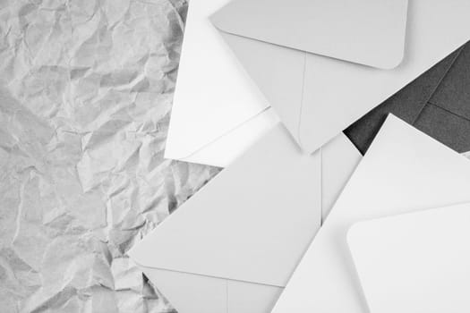 Monochrome background image of black and white cardboard envelopes lying randomly on crumpled paper background. Top view. Copy space