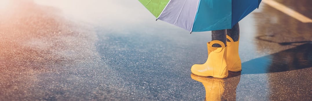 Child standing in the puddle in yellow rubber boots. Concept of childhood.