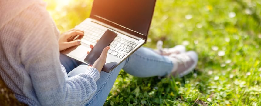 Woman with laptop sitting on the grass in the natural park. Concept of the freelance, working and learning.