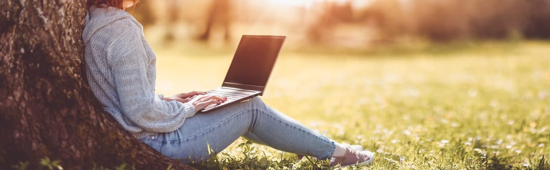 Woman with laptop sitting on the grass in the natural park. Concept of the freelance, working and learning.