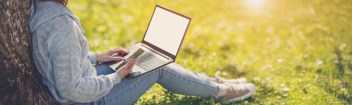 Woman with laptop sitting on the grass in the natural park. Concept of the freelance, working and learning.