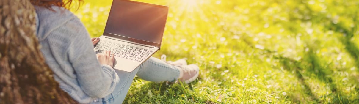 Woman with laptop sitting on the grass in the natural park. Concept of the freelance, working and learning.
