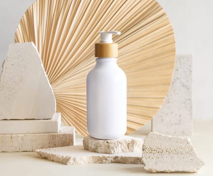 White One pump bottle on biege travertine stones against dried palm leaf, close up, mockup, copy space. Skincare beauty product. Eco friendly cosmetics