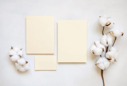 Blank paper cards with cotton flowers top view on white, mockup. Romantic scene with wedding or greeting cards set.