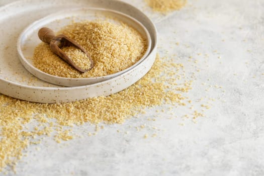Pile of Dry uncooked bulgur wheat grain with a scoop on a plate close up, copy space. Vegetarian and Vegan, Mediterranean and Middle Eastern cuisine. Healthy lifestyle