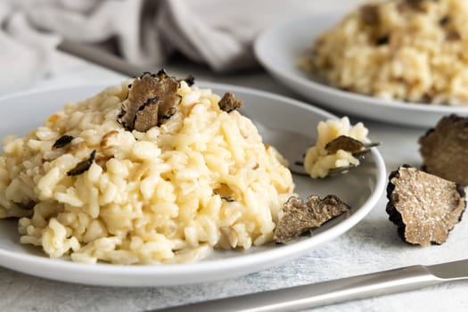 Risotto with wild porcini mushrooms and black truffles from Italy served in a plate close up on white table. Eating Italian gourmet cousine