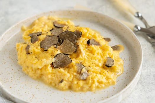 Scrambled eggs with sliced fresh black truffles from Italy served in a plate near fork and knife close up. Italian cousine, gourmet breakfast