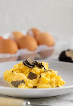 Scrambled eggs with sliced fresh black truffles from Italy served in a plate near fork and knife close up, copy space. Italian cousine, gourmet breakfast