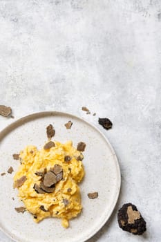 Scrambled eggs with sliced fresh black truffles from Italy served in a plate top view, copy space. Italian cousine, gourmet breakfast