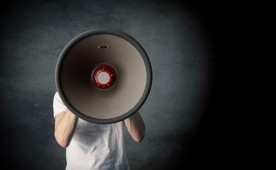 Young man holding a big megaphone, speaking loud concept on a dark studio background with space for your text or image