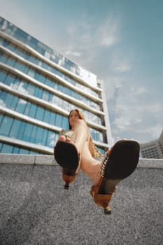 Bottom view of a woman sitting on a marble fence illuminated by a sun-soaked sky. Low angle view at soles of female sandals