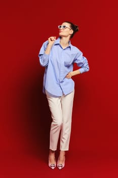 Woman in cotton shirt and trousers on deep red background looks up