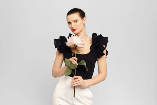 Stylish and positive adult woman posing in white studio with rose in hands