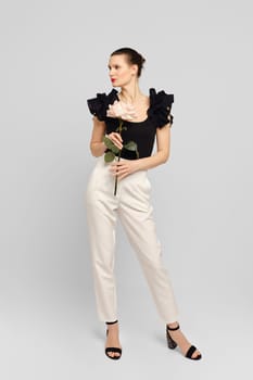 Stylish adult woman posing in white studio with flower in hands