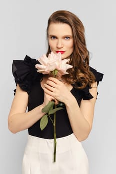 Medium closeup studio portrait of cute woman sniffs beautiful flower