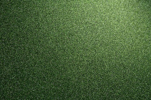 Deep grassy green. Texture of rough paper or cardboard. Defocused bokeh sparkles and shine on the fold. Festive green background with illuminated gradient from top right