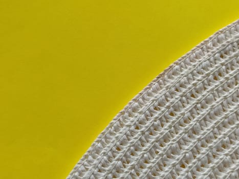 Straw hat on a yellow background. The edge of the wide brim of the hat. Weave threads or twigs. Close-up. Summer holiday theme.