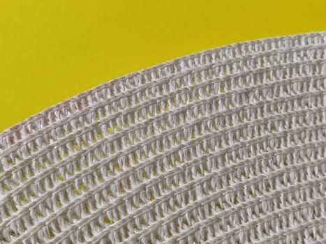 Straw hat on a yellow background. The edge of the wide brim of the hat. Weave threads or twigs. Close-up. Summer holiday theme.
