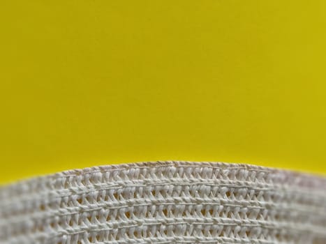Straw hat on a yellow background. The edge of the wide brim of the hat. Weave threads or twigs. Close-up. Summer holiday theme.