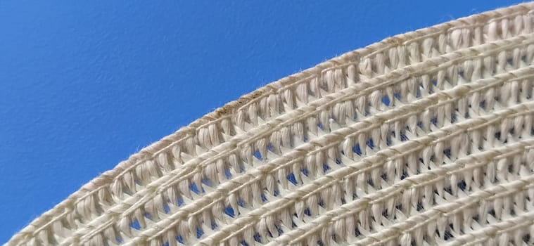 Straw hat on a blue background. The edge of the wide brim of the hat. Weave threads or twigs. Close-up. Summer holiday theme. Banner.