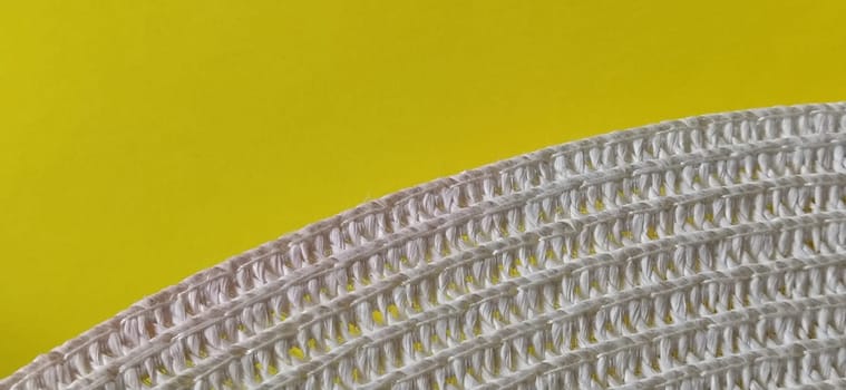 Straw hat on a yellow background. The edge of the wide brim of the hat. Weave threads or twigs. Close-up. Summer holiday theme.