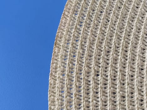 Straw hat on a blue background. The edge of the wide brim of the hat. Weave threads or twigs. Close-up. Summer holiday theme.