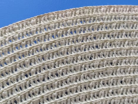 Straw hat on a blue background. The edge of the wide brim of the hat. Weave threads or twigs. Close-up. Summer holiday theme.