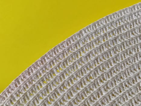 Straw hat on a yellow background. The edge of the wide brim of the hat. Weave threads or twigs. Close-up. Summer holiday theme.