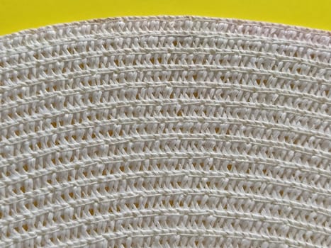 Straw hat on a yellow background. The edge of the wide brim of the hat. Weave threads or twigs. Close-up. Summer holiday theme.